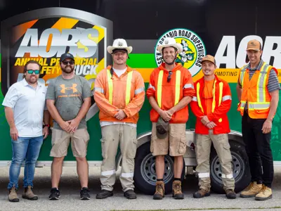 City staff in bright orange vests pose in front of a Association of Ontario Road Supervisors (AORS) sign