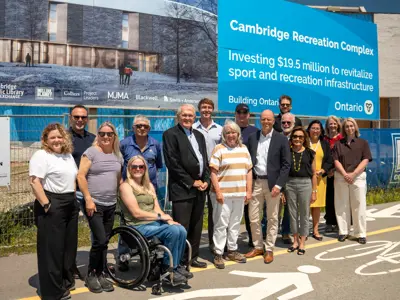 A group of City Council members, City staff and Gore Mutual representatives pose in front of a large project sign for the Cambridge Recreation Complex at the construction site before a guided tour.