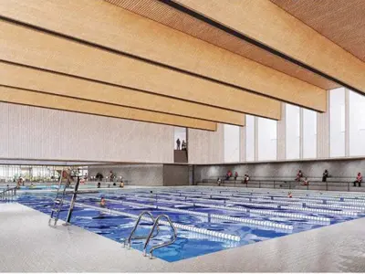 Architectural rendering of the future aquatics facility at the Cambridge Recreation Centre. The bright, modern indoor pool features multiple lap lanes with lane markers, accessible entry points with stainless steel handrails, spectator seating along one side, and large windows that bring natural light into the space. Wood-accented ceiling panels and clean, contemporary finishes create an open and welcoming environment.
