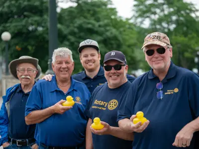 Five Rotary Club members stand together outdoors at the Goose on the Grand event, each holding a small yellow rubber duck purchased for the duck race.