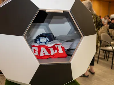 A soccer ball-shaped display case contains Galt Football Club memorabilia, including a red sweater with "GALT" across the front, a cap, and other items.